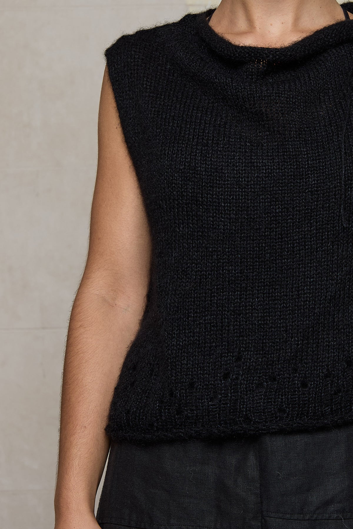 Close up fabric view of super lush knitted vest in black. Vest features random laceholes along hemline.