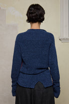 Backview of model wearing wool boucle knitted jumper in blue with orange external seams.