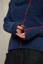 Close up fabric view of wool boucle knitted jumper in blue with orange external seams.