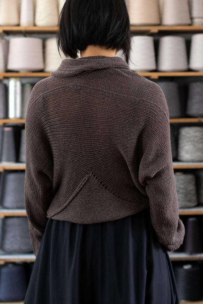 Model is standing in front of a shelf of yarns, showing the back view of a chunky knit merino wool jumper in taupe, designed and made in Melbourne by Wendy Voon