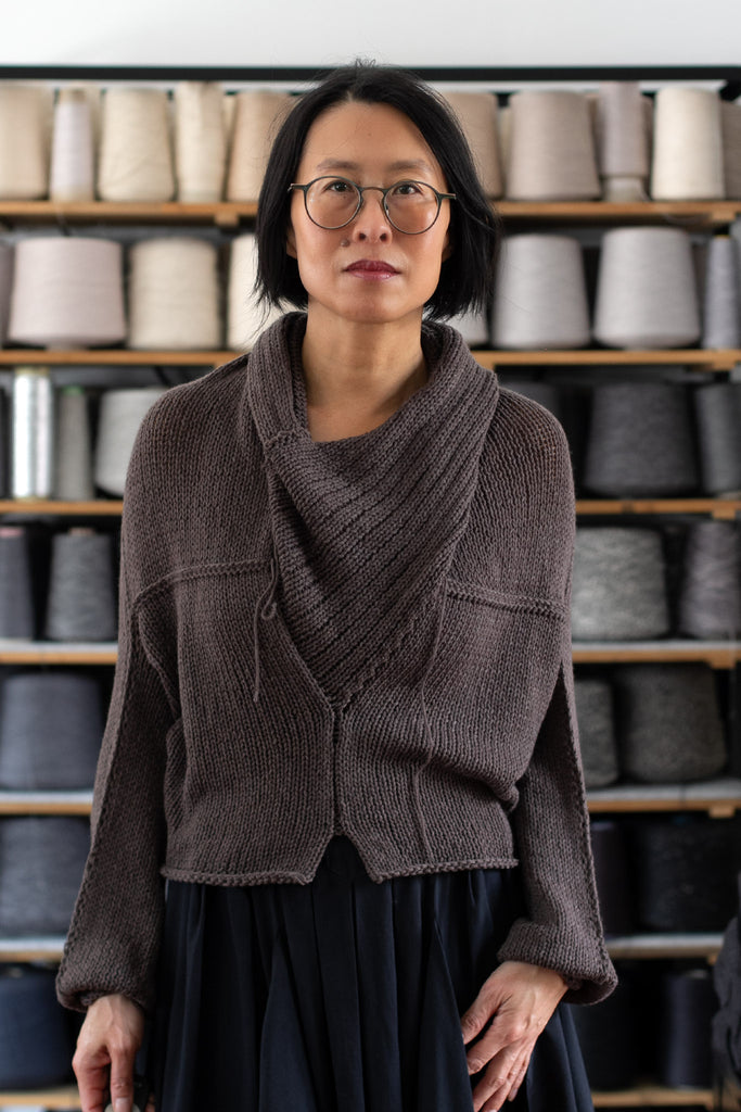Model is standing in front of a shelf of yarns, wearing a chunky knit merino wool jumper in taupe, designed and made in Melbourne by Wendy Voon
