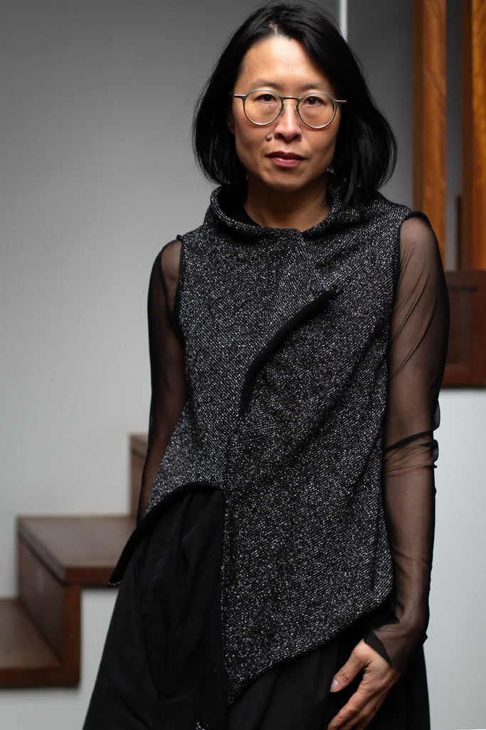 Model wears asymmetric self curling vest, in a silver metallic backed with black merino wool fabric.