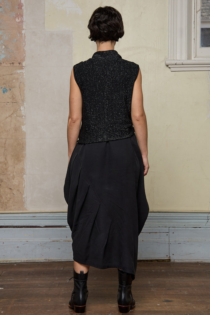 Back view of model wearing asymmetric self-curling vest in silver metallic on black merino wool vest, tied at the front. 