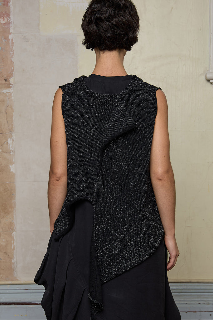 Back view of model wearing asymmetric self-curling vest back to front, in silver metallic on black merino wool vest.