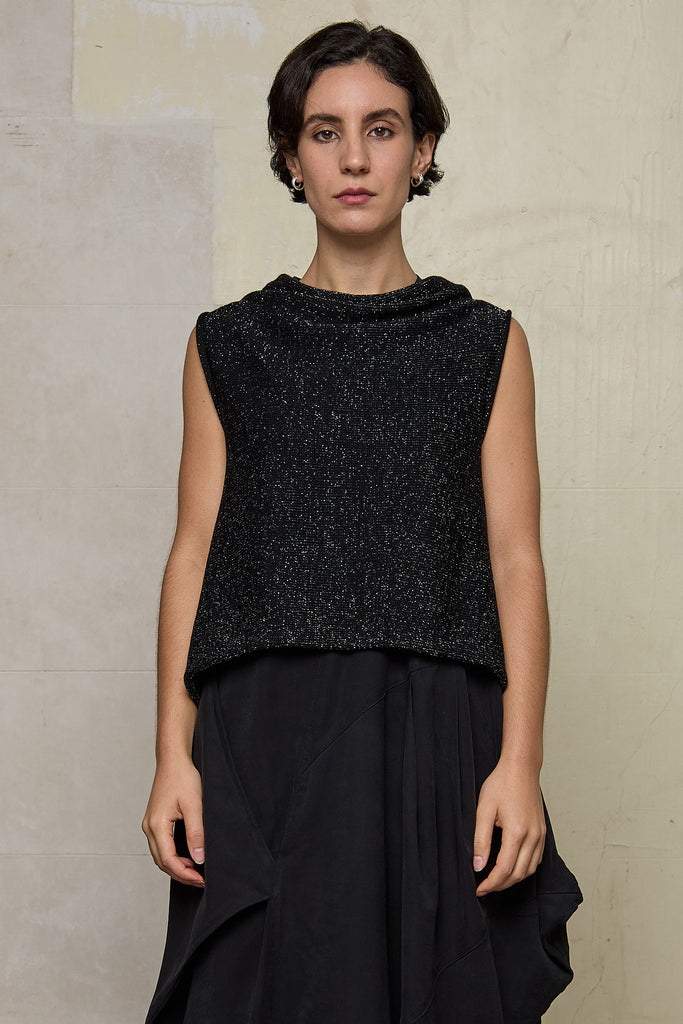 Model wears asymmetric self-curling vest back to front in silver metallic on black merino wool vest.