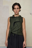 Model wears knitted asymmetric self-curling vest cinched at the waist, in army green on black colourway.
