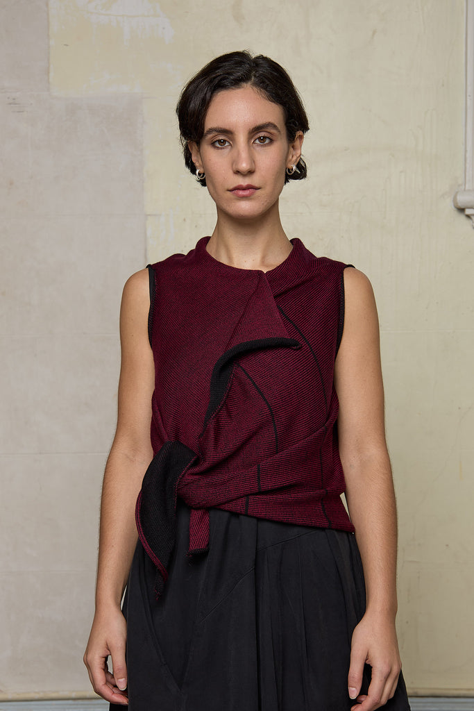 Model wears knitted asymmetric self-curling vest, cinched at the waist, in burgundy on black colourway. Designed and knitted in Melbourne by Wendy Voon knits