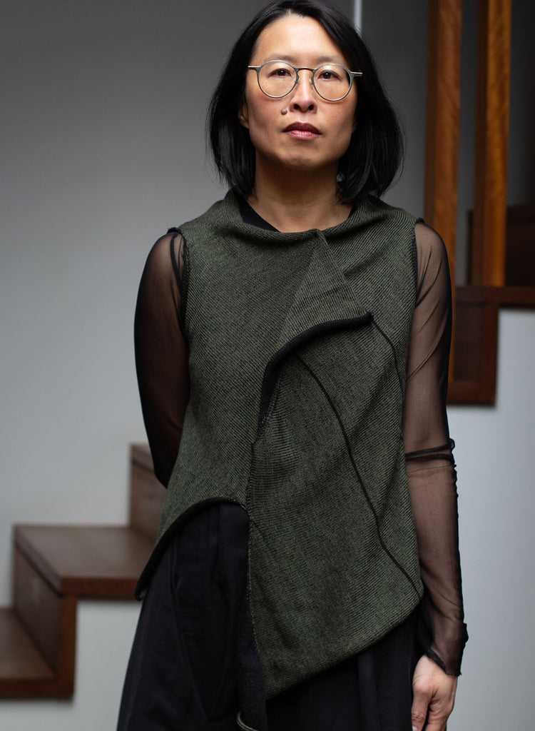 Model wears an asymmetric self-curling vest, knitted in superfine merino wool,in an army backed with black colourway, designed and knitted in Melbourne by Wendy Voon knits.