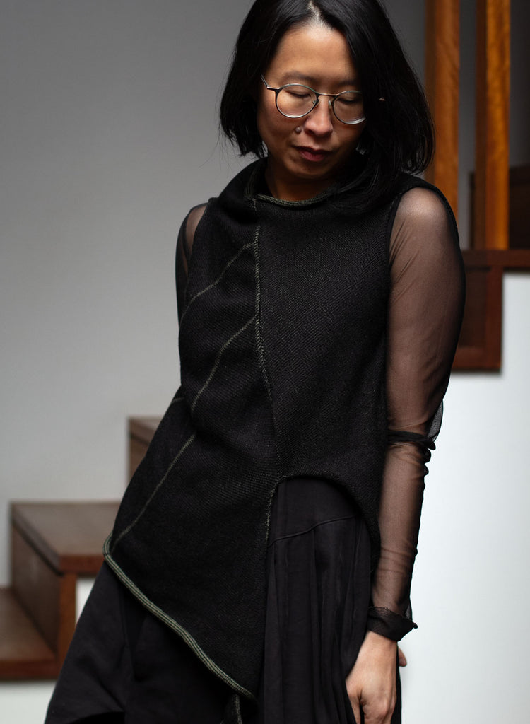 Model wears an asymmetric self-curling vest inside out, knitted in superfine merino wool,in an army backed with black colourway, designed and knitted in Melbourne by Wendy Voon knits.