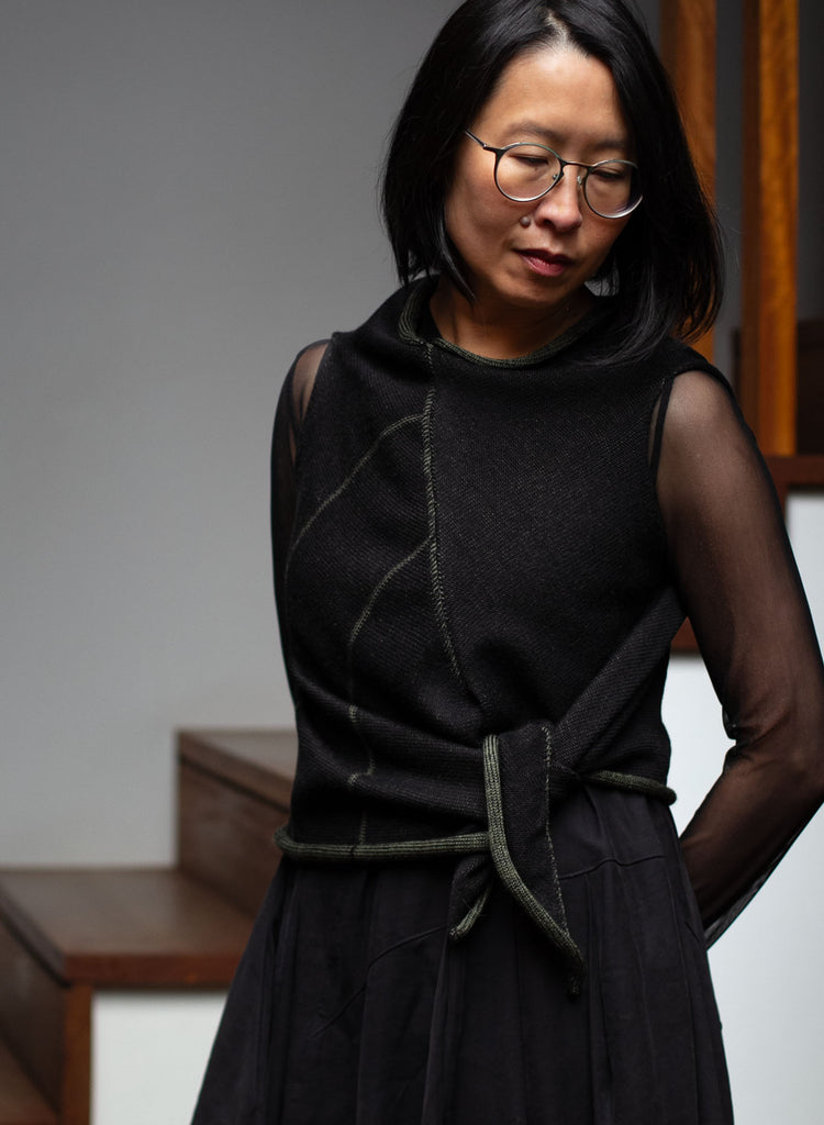 Model wears an asymmetric self-curling vest inside out and tied at the waist. Vest is knitted in superfine merino wool,in an army backed with black colourway, designed and knitted in Melbourne by Wendy Voon knits.