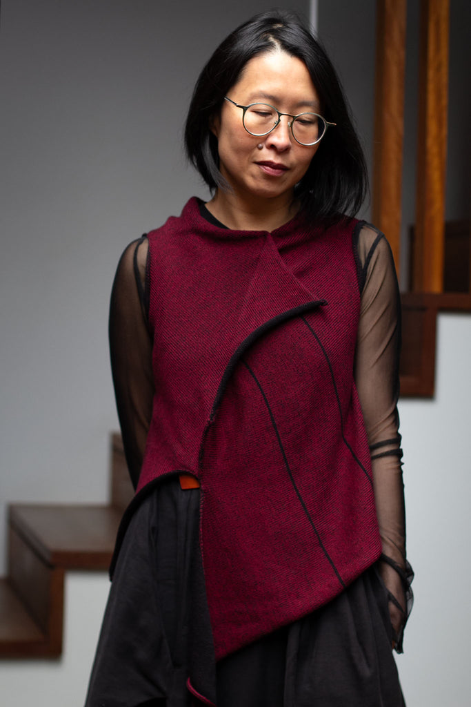 Model wears an asymmetric self-curling vest back to front.  Vest is knitted in superfine merino wool,in a maroon backed with black colourway, designed and knitted in Melbourne by Wendy Voon knits.