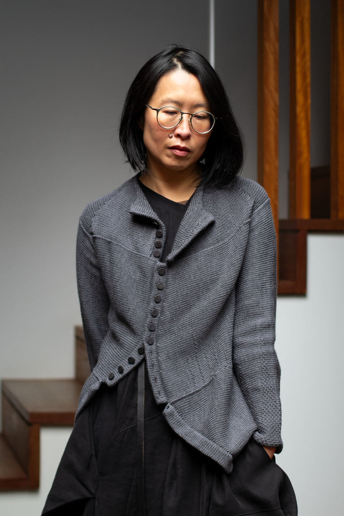Model wears knitted steel grey peplum riding coat, featuring many small buttons, and made from a chunky superfine merino yarn. This piece is designed and made in Melbourne by Wendy Voon knits. 