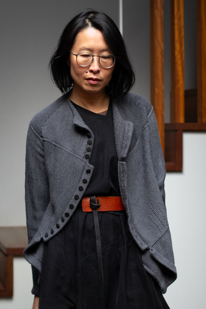 Model wears knitted steel grey peplum riding coat, featuring many small buttons that are undone, and made from a chunky superfine merino yarn. This piece is designed and made in Melbourne by Wendy Voon knits. 