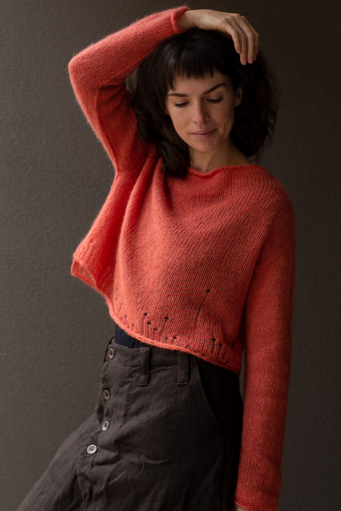Three quarter front view of super soft knitted jumper in a carrot colour way, featuring laddered laceholes, made from baby alpaca, mohair and silk. Designed and made in Melbourne by Wendy Voon knits