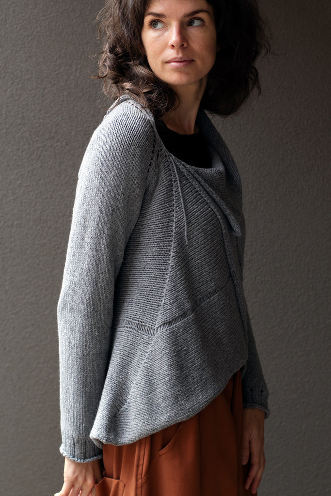 Side view of  superfine merino wool/polyamide soft grey jumper, designed by Wendy Voon knits, made in Melbourne.  Jumper features triangular panels at front with loose threads left as design feature