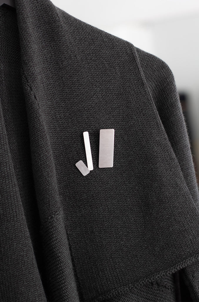 A set of three stainless steel rectangular brooches of different sizes, on a woollen cardigan