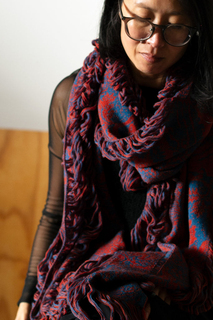 Model wears wool damask patterned scarf in a rust and lagoon colourway. Designed by Wendy Voon and made in Melbourne.